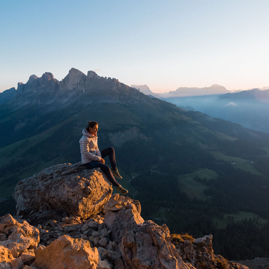 Hiker sitting on a rock in golden light overlooking the Dolomites
